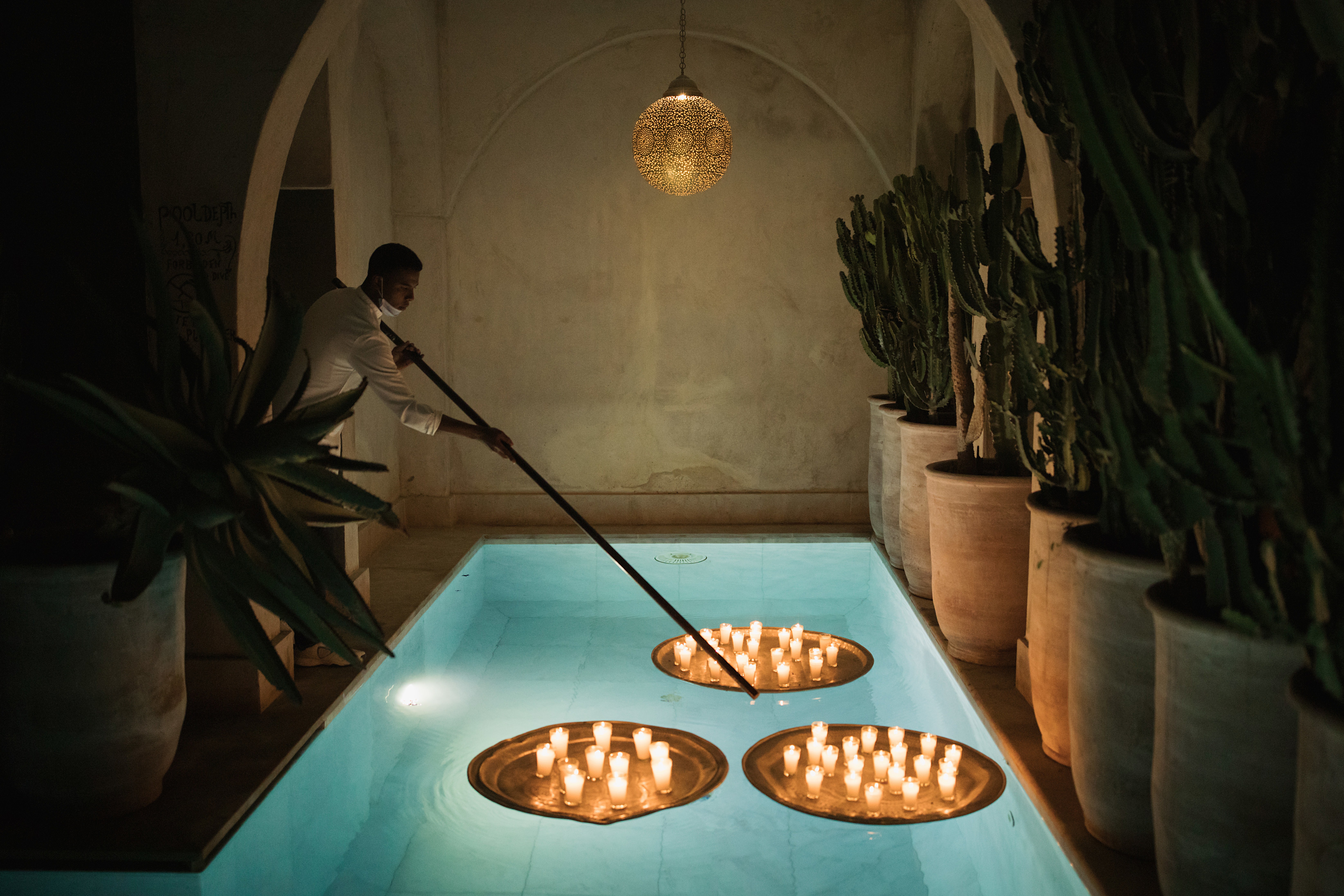 A candlelit hotel spa indoor pool is decorated with floating golden trays filled with candles and tall ceramic vases with cacti.