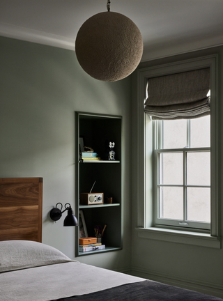 A bedroom with a dark-toned green wall paint, a beige overhead light, and gray bedding