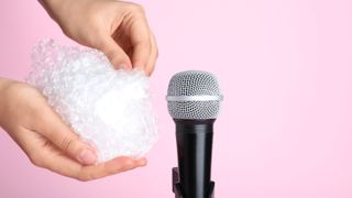 woman making ASMR sounds with microphone and bubble wrap on pink background