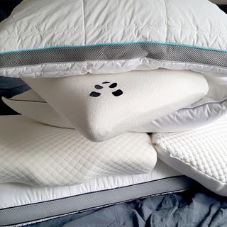 A group of pillows of different shapes and sizes on a bed with grey linen bedding