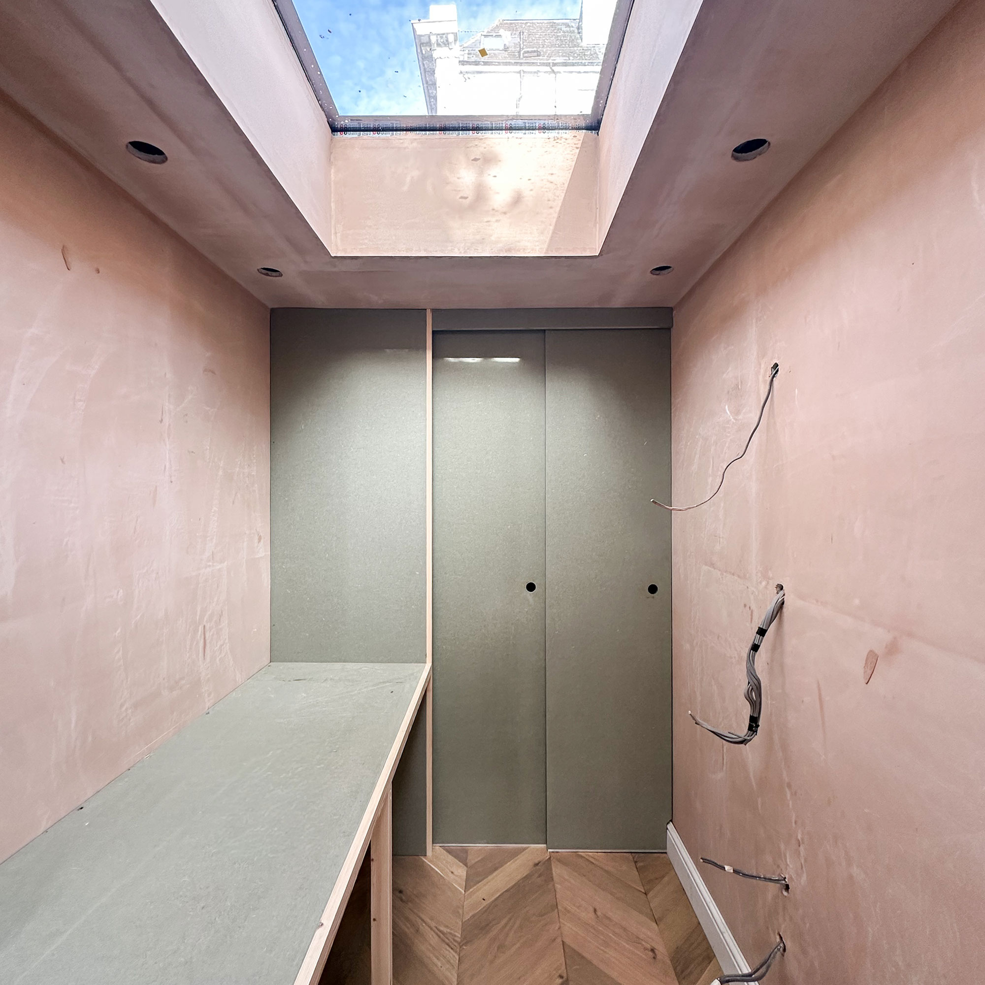 Empty room with plaster walls, exposed wiring, wooden parquet flooring, skylight and green pocket door