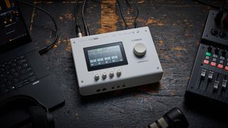 A Yamaha URX44V audio interface on a worn wooden surface with a laptop and a mixing desk