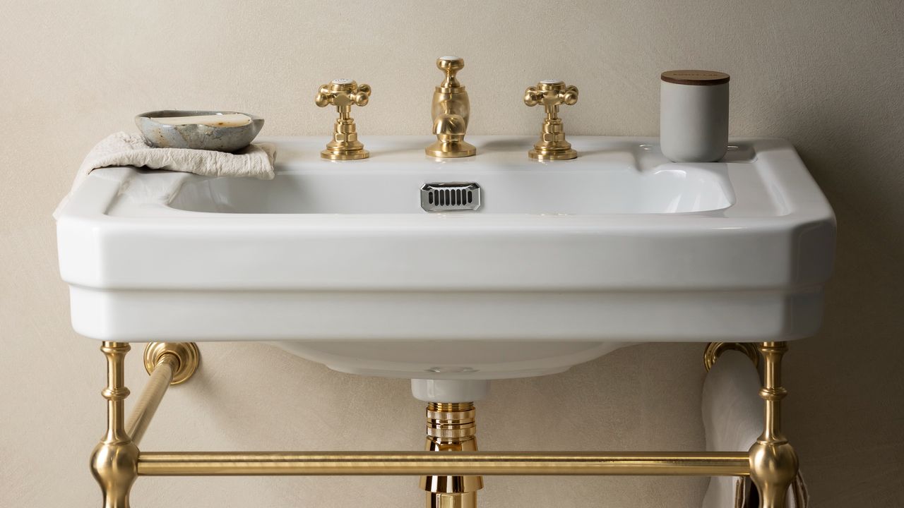 Two gold taps with gold separator on white sink with gold frame underneath