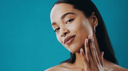 Woman pictured against a blue background with glowing skin caresses her skin