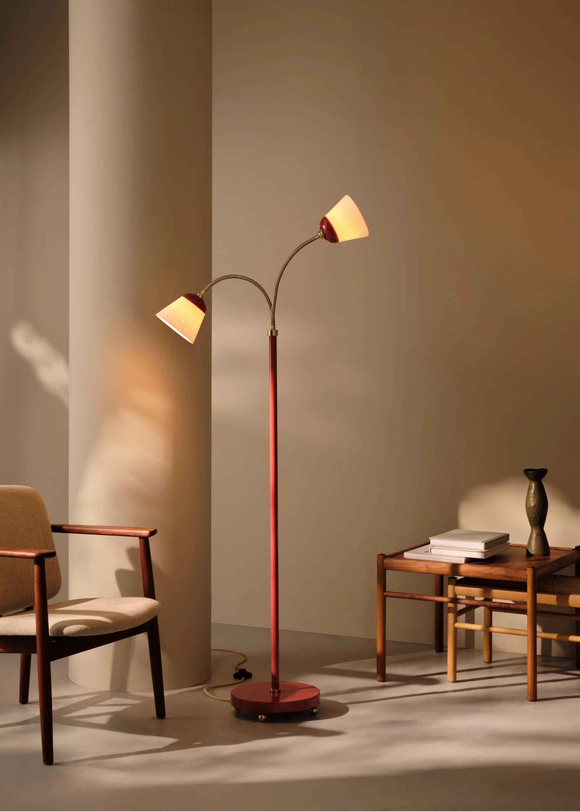A red colored floor lamp with two lamp heads next to a chair and a side table.