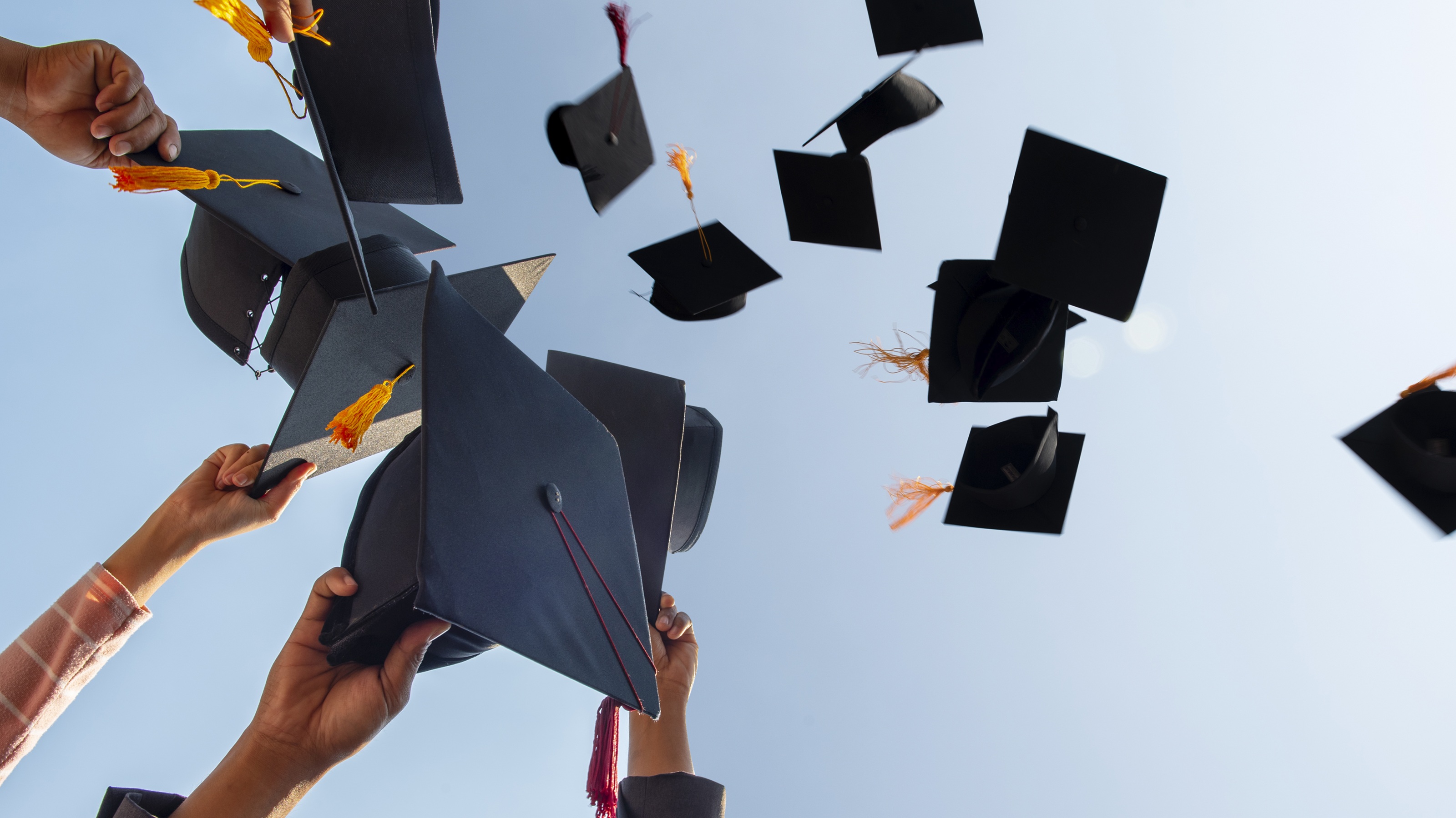 Graduates' mortar boards fly through the air against a blue sky.