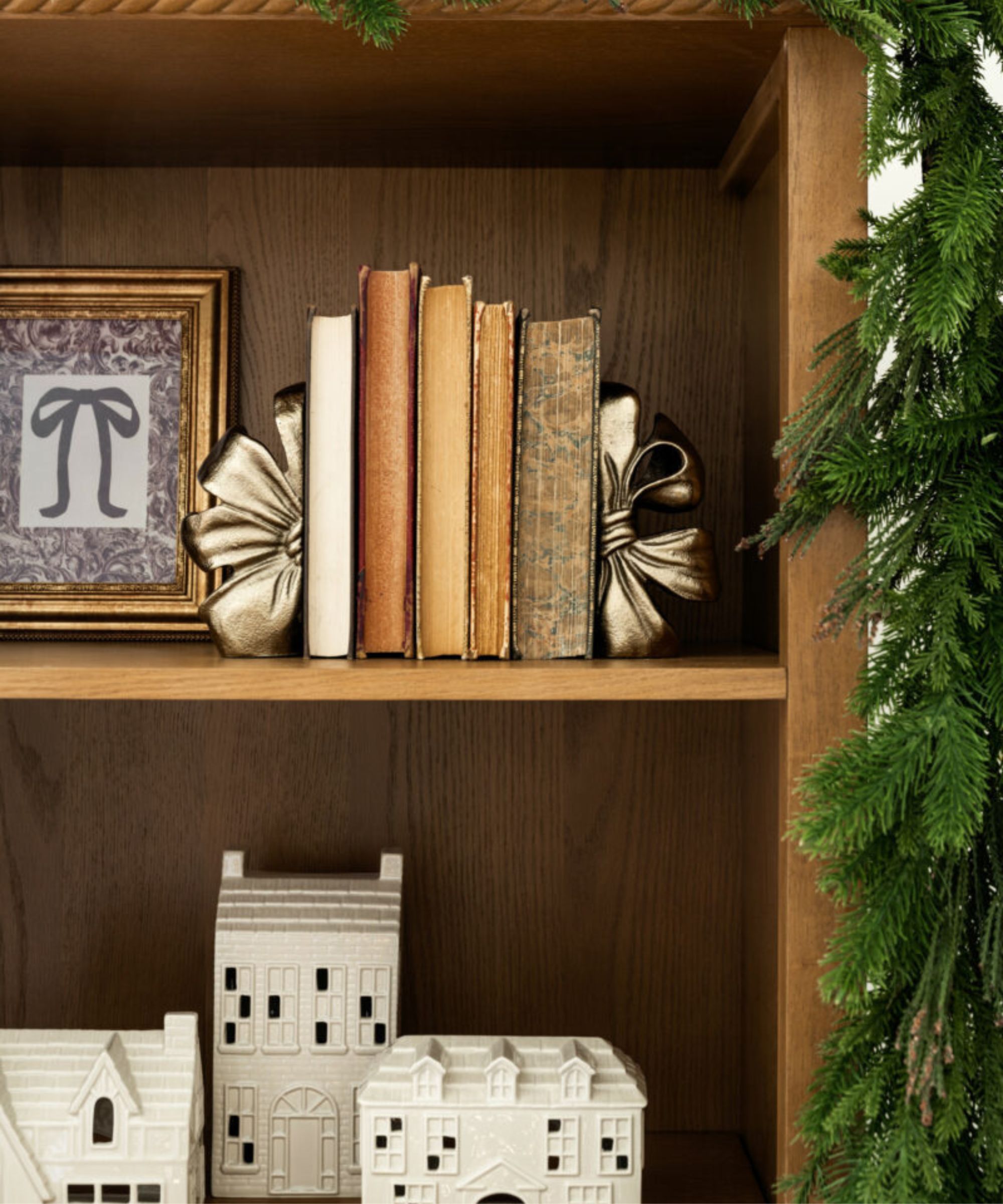 Wooden bookcase with old books, bow book ends, framed print and ceramic houses
