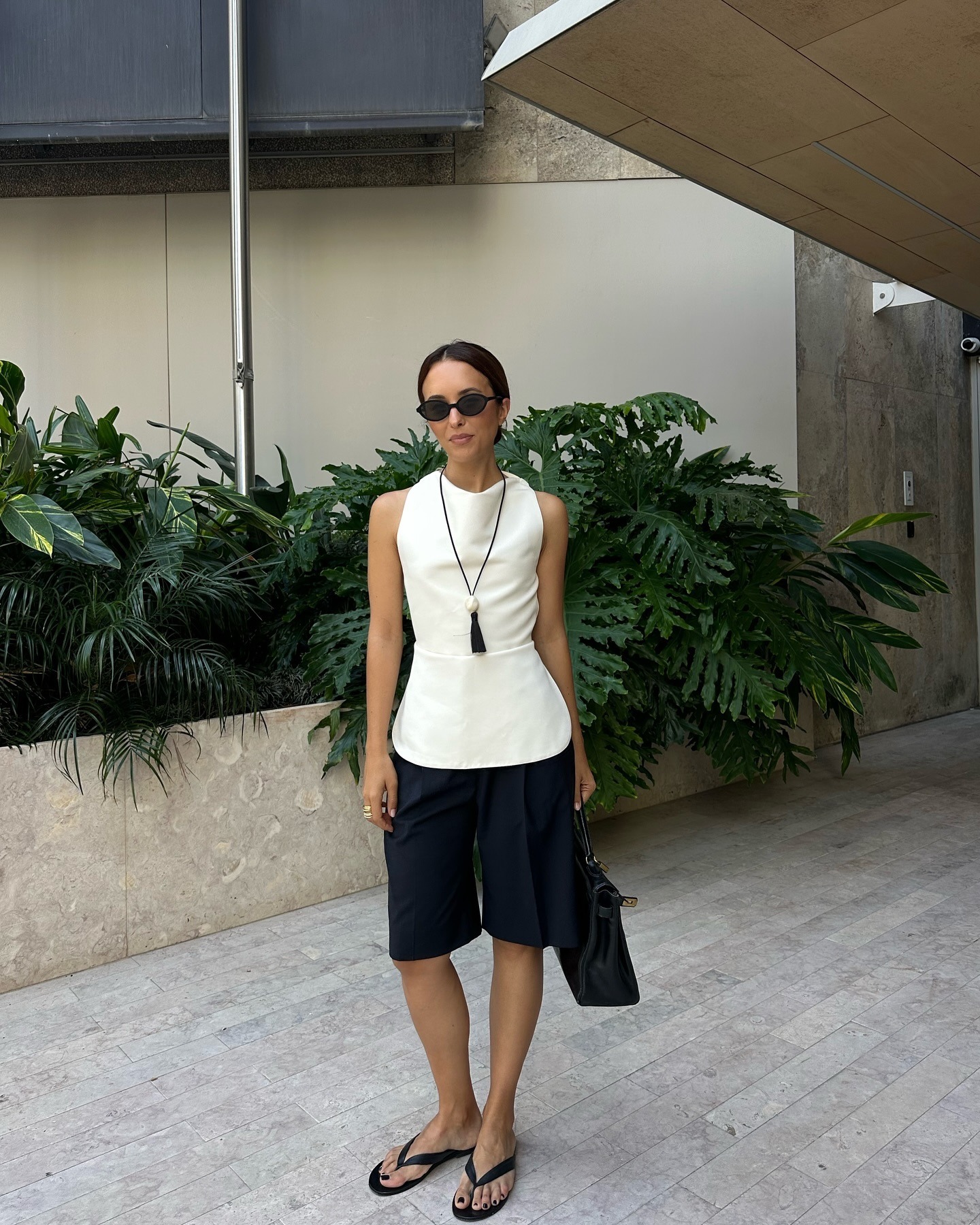 The woman is wearing a cream-colored top, black shorts, and black flip-flops.