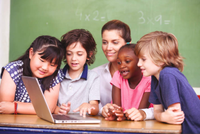 A group of students sit around a classroom table starring at a laptop.