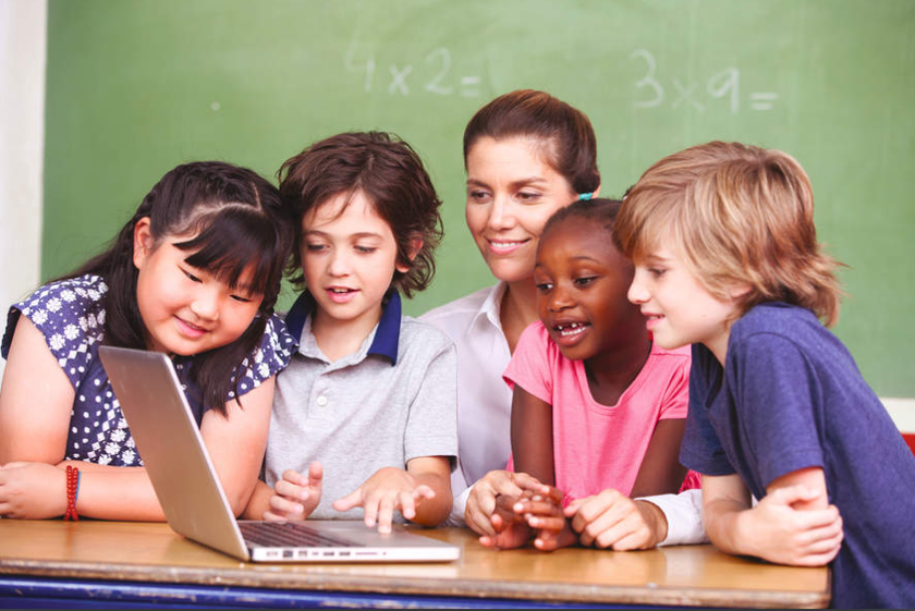 A group of students sit around a classroom table starring at a laptop.