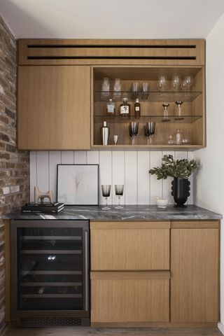 A modern home bar with wooden slab cabinets, a granite countertop, and an exposed brick wall