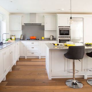 A white kitchen with wooden flooring and a grey splashback