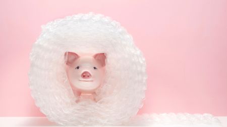 Piggy bank wrapped in bubble pack on white shelf, pink background