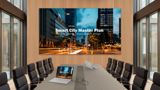 A dvLED display at the head of a conference roo, table showing city plans. 