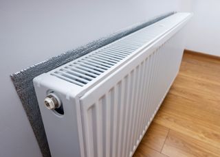 White metal heating radiator forming part of a central heating system with energy-efficient thermal insulation on the wall