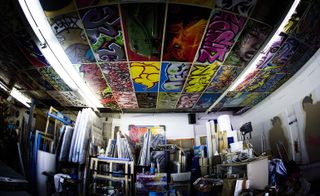 Art room is filled with canvases and graffiti on the ceiling.
