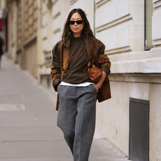 Sophia Geiss is seen wearing a white oversized shirt with subtle vertical stripes, a chest pocket and wide cuffs from Black Palms; cream white knee-length bermuda shorts with an oversized fit and front pleats from Eme Studios; black kitten heel thong sandals with a minimalist flip-flop silhouette and low heel from Leger by Lena Gercke; a soft ivory shoulder city bag with a folded flap, elongated shape and knotted strap details from comma Fashion; a silver chunky cuff bracelet worn above the shirt sleeve from COS; her brown hair is styled in a sleek low bun on July 27, 2025 in Berlin
