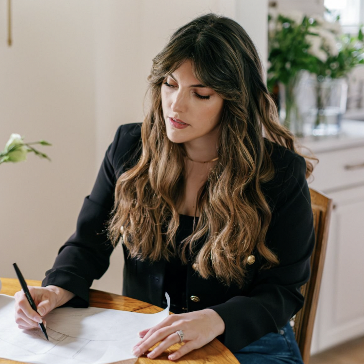 A woman with long brown hair sat at a desk drawing