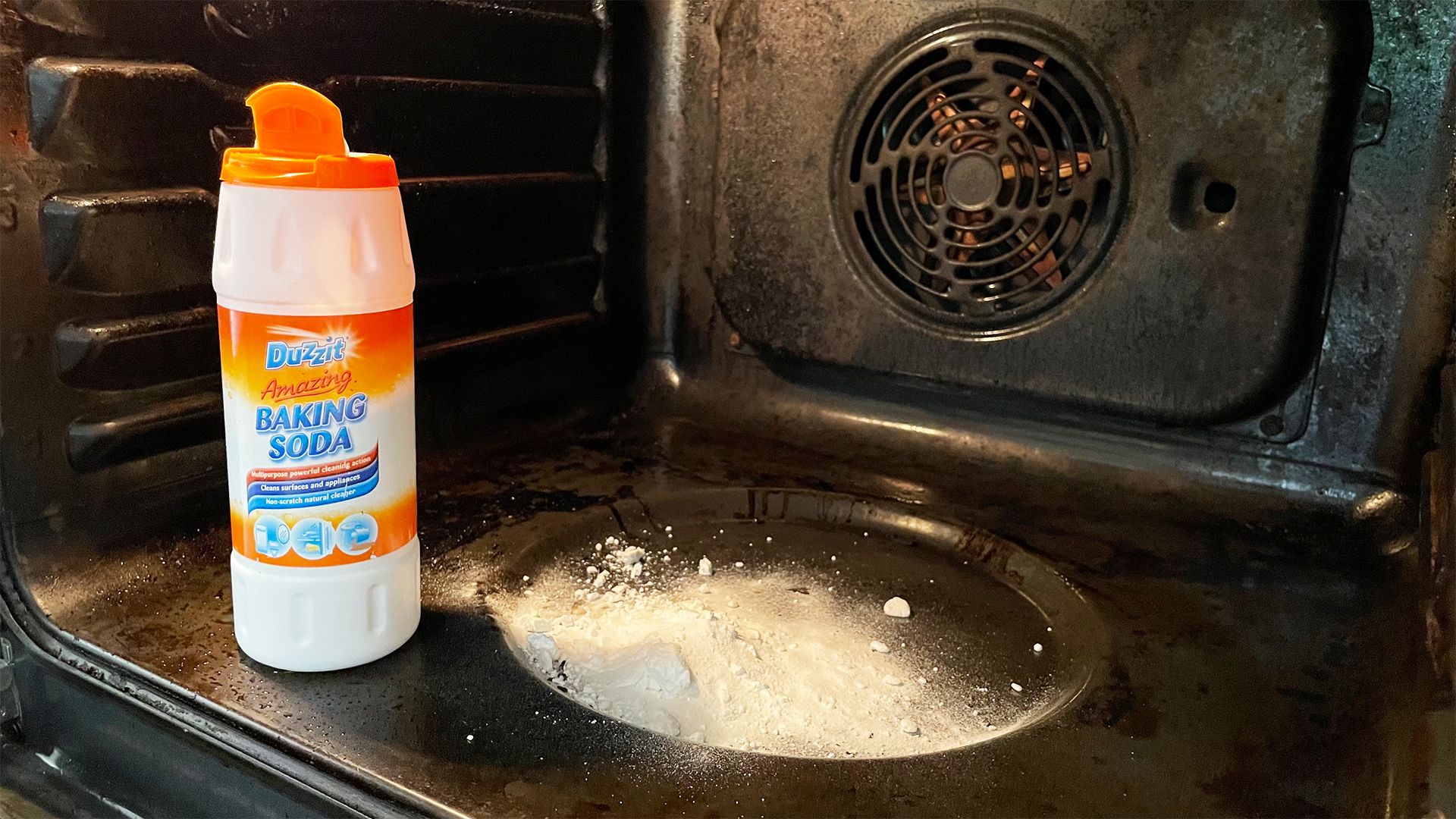 Dirty oven with a bottle of baking soda sitting inside with some product poured onto the base of the oven