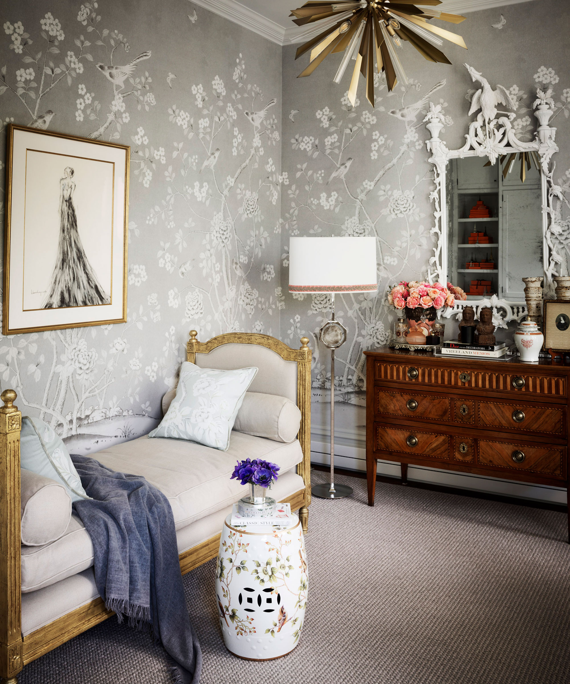 A pale gray wallpapered dressing room with gold and cream chaise and wooden dressing table with white baroque style mirror.