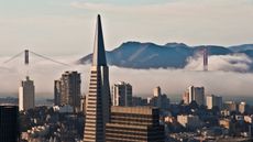 An aerial photo of San Francisco with the Transamerica tower in the foreground and mountains in the background.