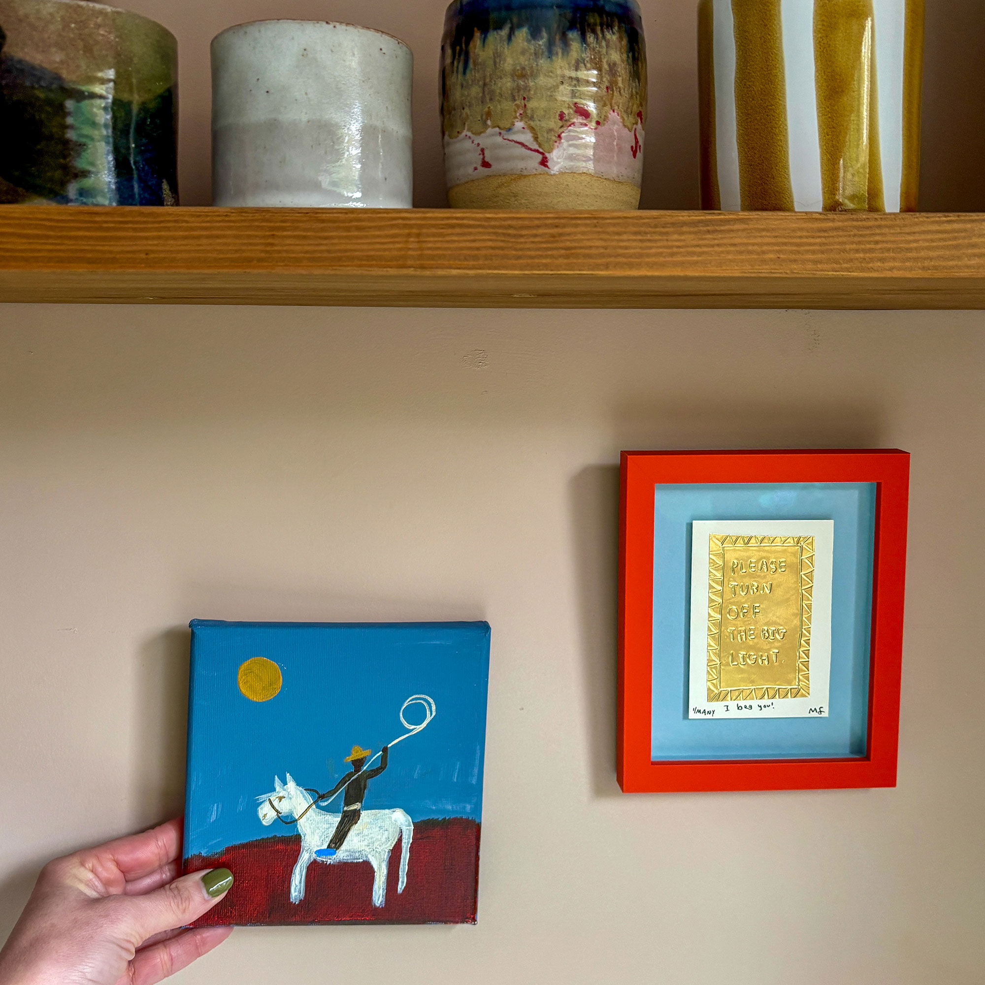 Woman holding up small painting against wall