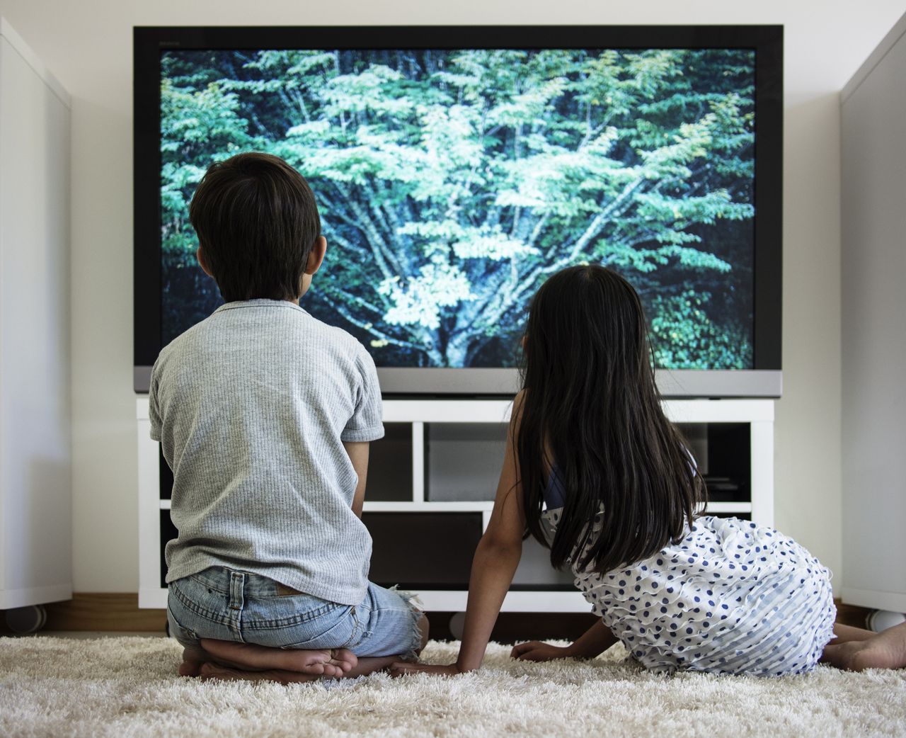 two children sitting in front of a tv screen which is lit up with blue-green light.