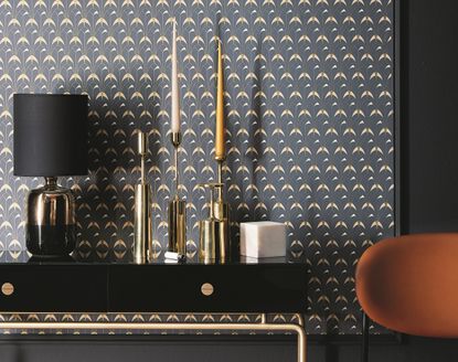 A room with art deco style wallpaper and candles in gold holders on a mantelpiece
