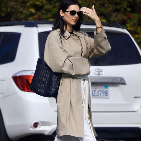 Kendall Jenner wearing a long silk scarf around her waist with a trench coat, white jeans, and ballet flats.