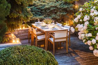 illuminated patio area with wooden furniture and hedges