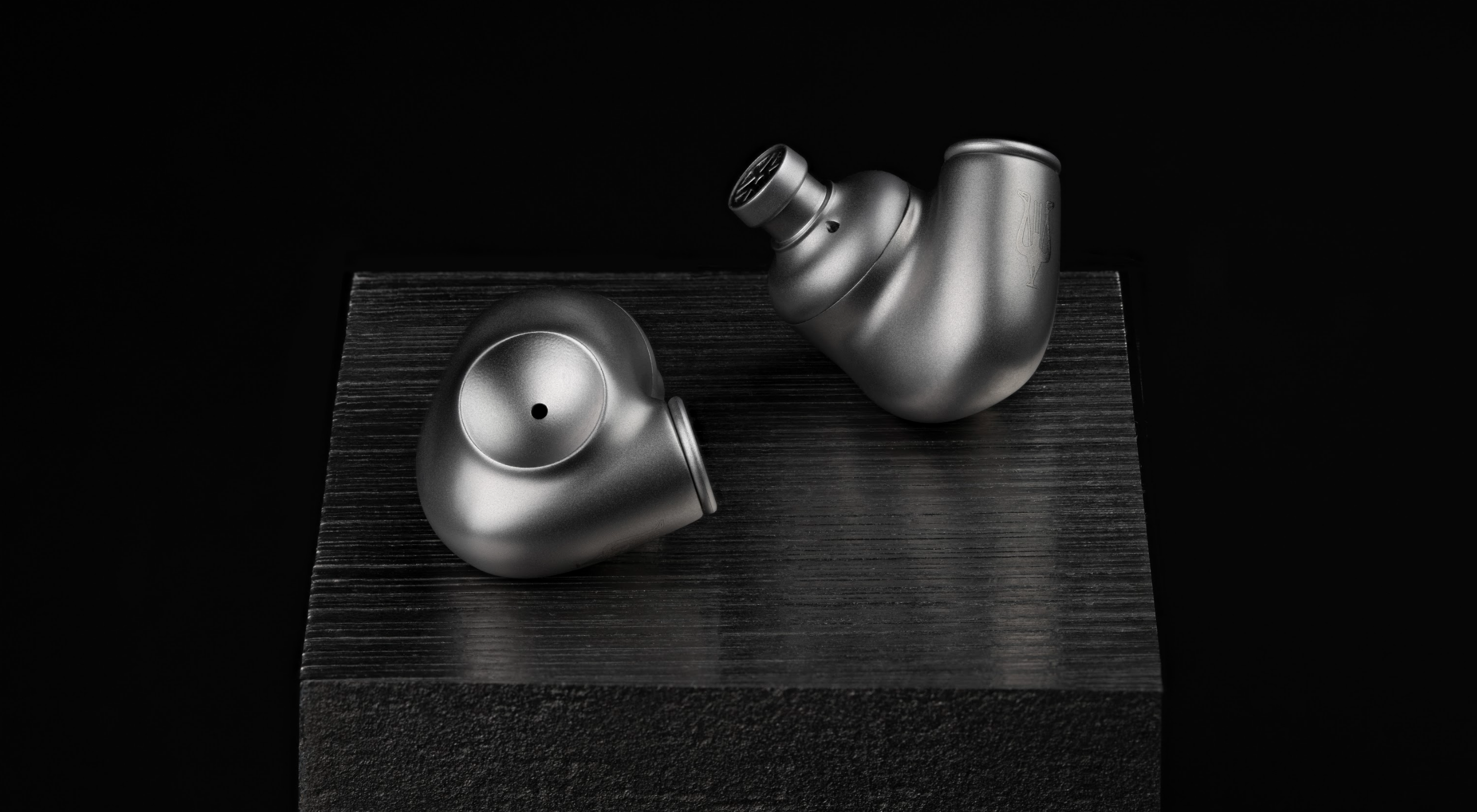 Meze Audio Astru IEMs without cable or ear tips, on a black plinth