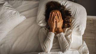 Woman lying in bed covering her face with her hands