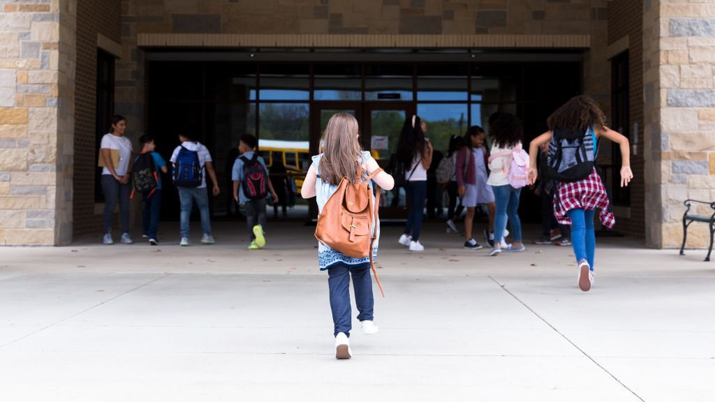 group of school children with backpacks on running toward the entrance of a school building