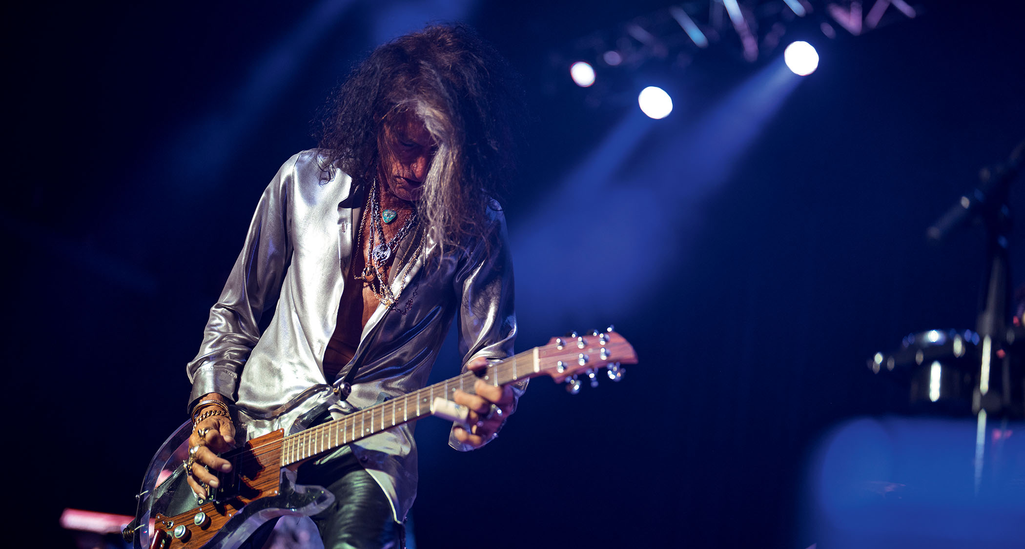 Joe Perry wears a silver shirt and plays his see-through Dan Armstrong live onstage.