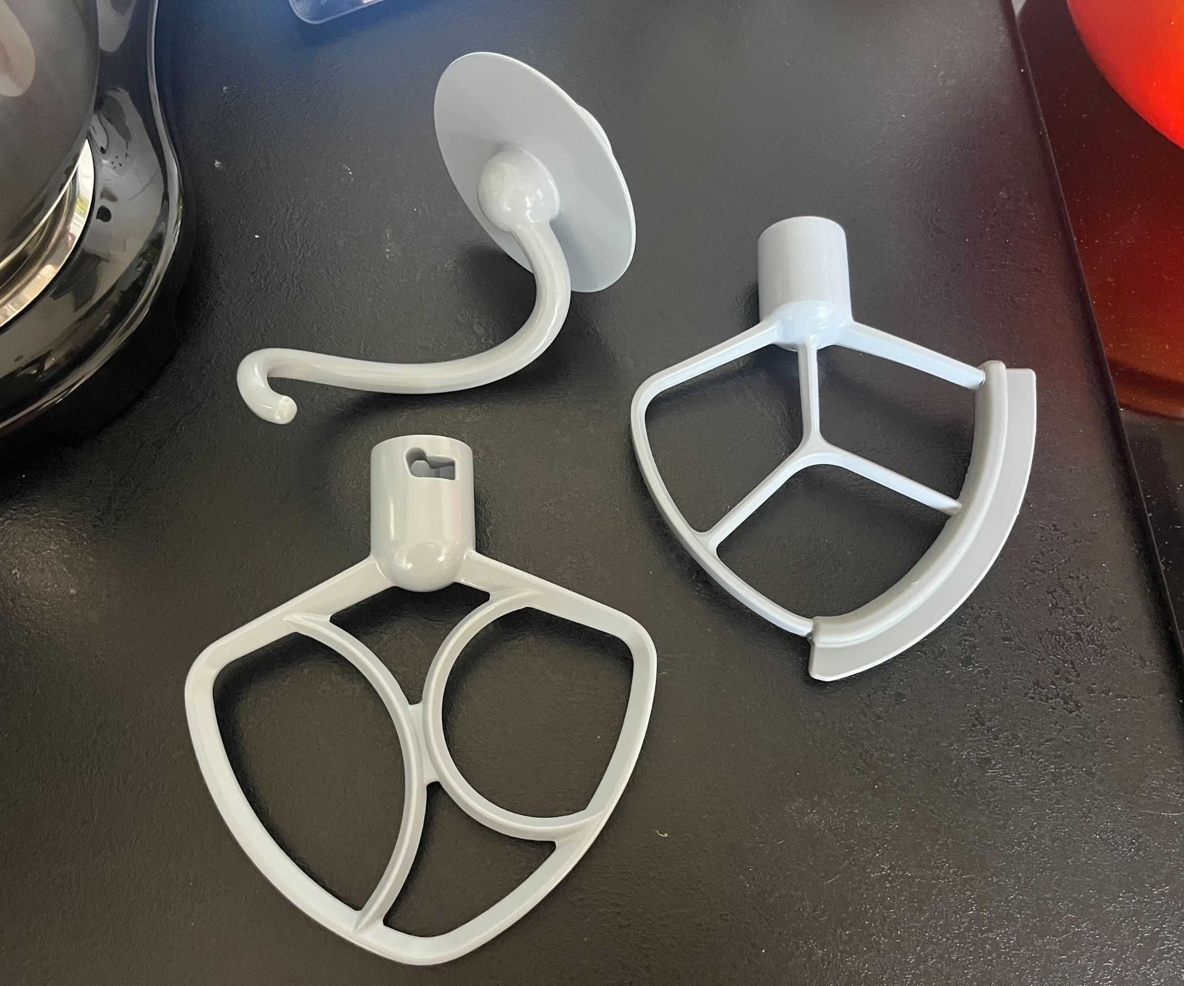 The grey steel paddle and dough hook attachments for the SMEG stand mixer on a black kitchen counter.