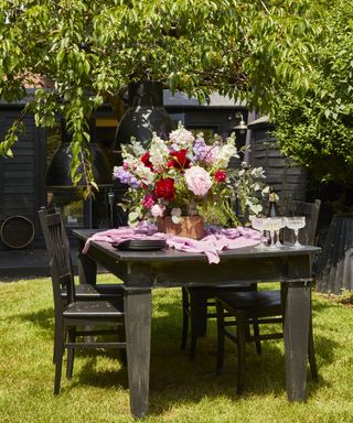 A vintage table and chairs used as a garden table with a bouquet of cut flowers