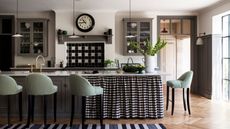 A black and white kitchen with a black and white checked curtained island and green checked bar stools.