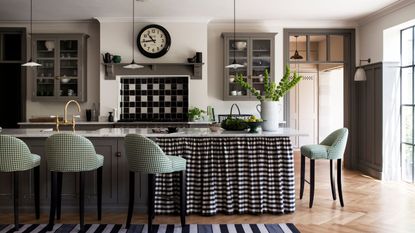 A black and white kitchen with a black and white checked curtained island and green checked bar stools. 