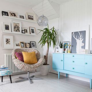 room with white wall and photo gallery and wooden floor and blue drawer unit and arm chair