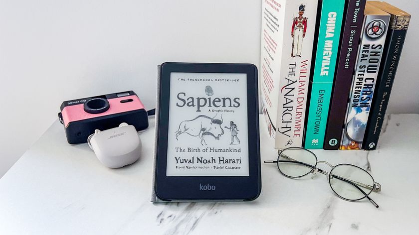 Kobo Clara BW op een tafel met boeken, een bril, een camera en een paar draadloze oortjes ernaast