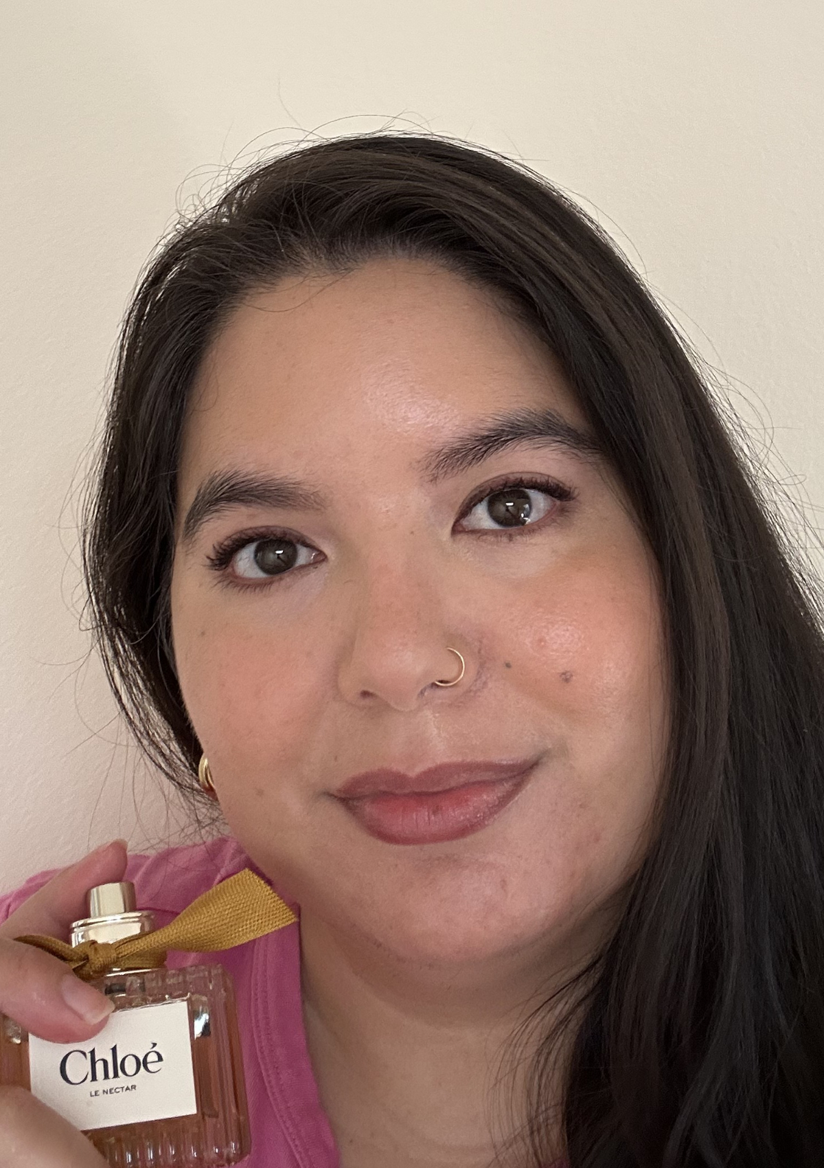 Me holding Chlo&amp;eacute; Le Nectar perfume, pink top and loose hair with a soft everyday makeup look and rosy nude lips