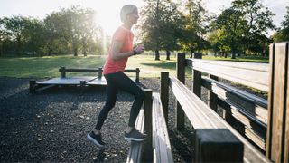 Woman doing step ups on a bench in a local park wearing workout clothes and headphones