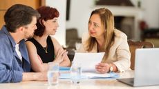 A couple look at paperwork held by a financial adviser at her desk in her office.