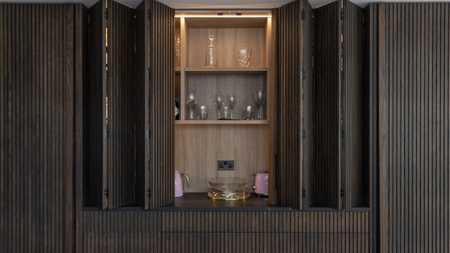 led lighting strip behind a wooden kitchen bifolding door with open shelving and pink smeg appliances within