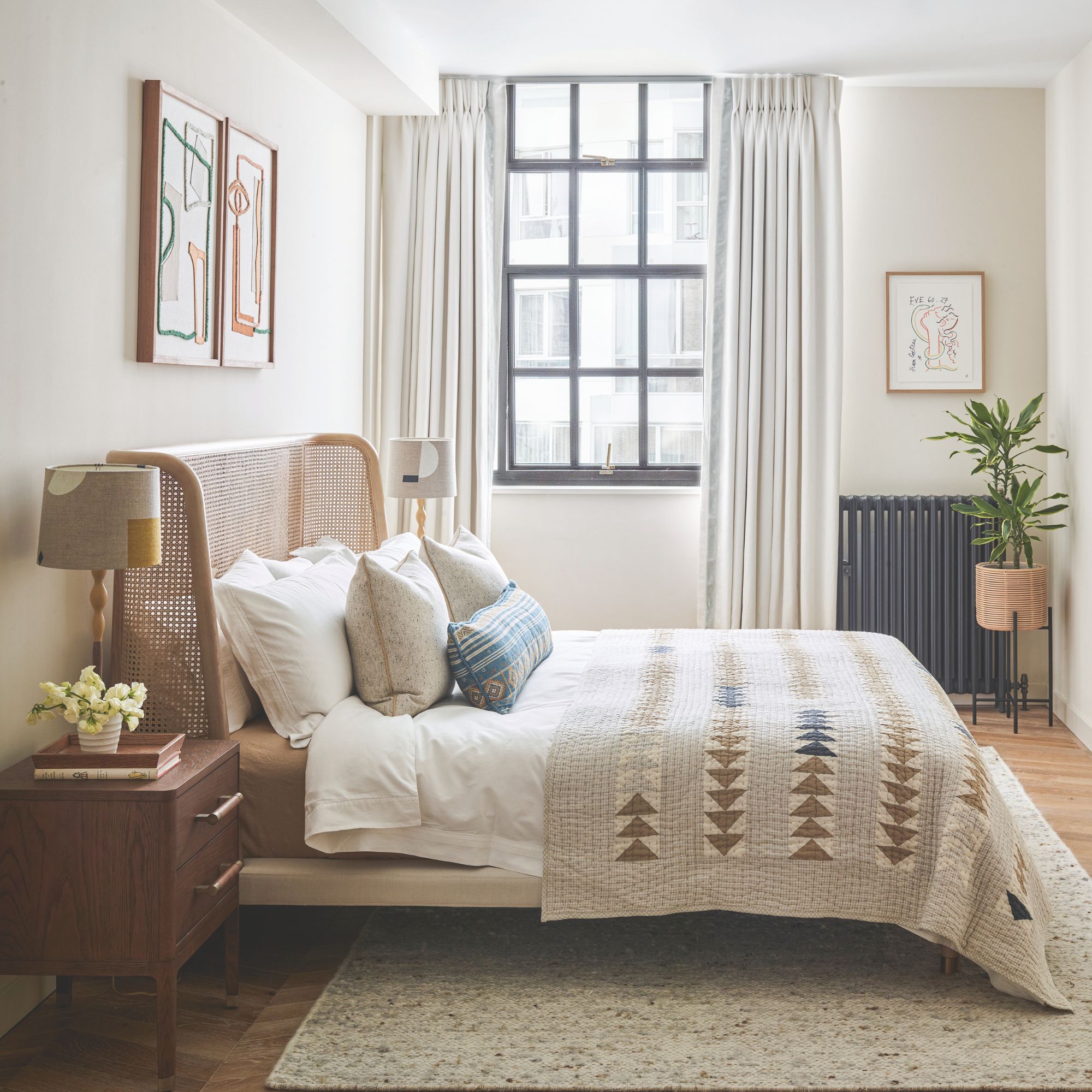 Neutral bedroom with rattan headboard, black radiator, wooden bedside table and black window