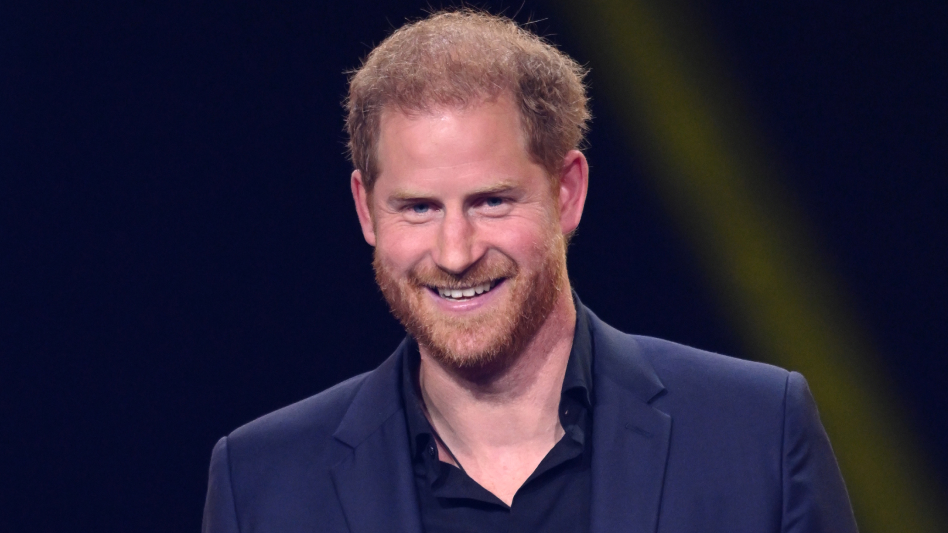 Prince Harry smiles while wearing a navy suit