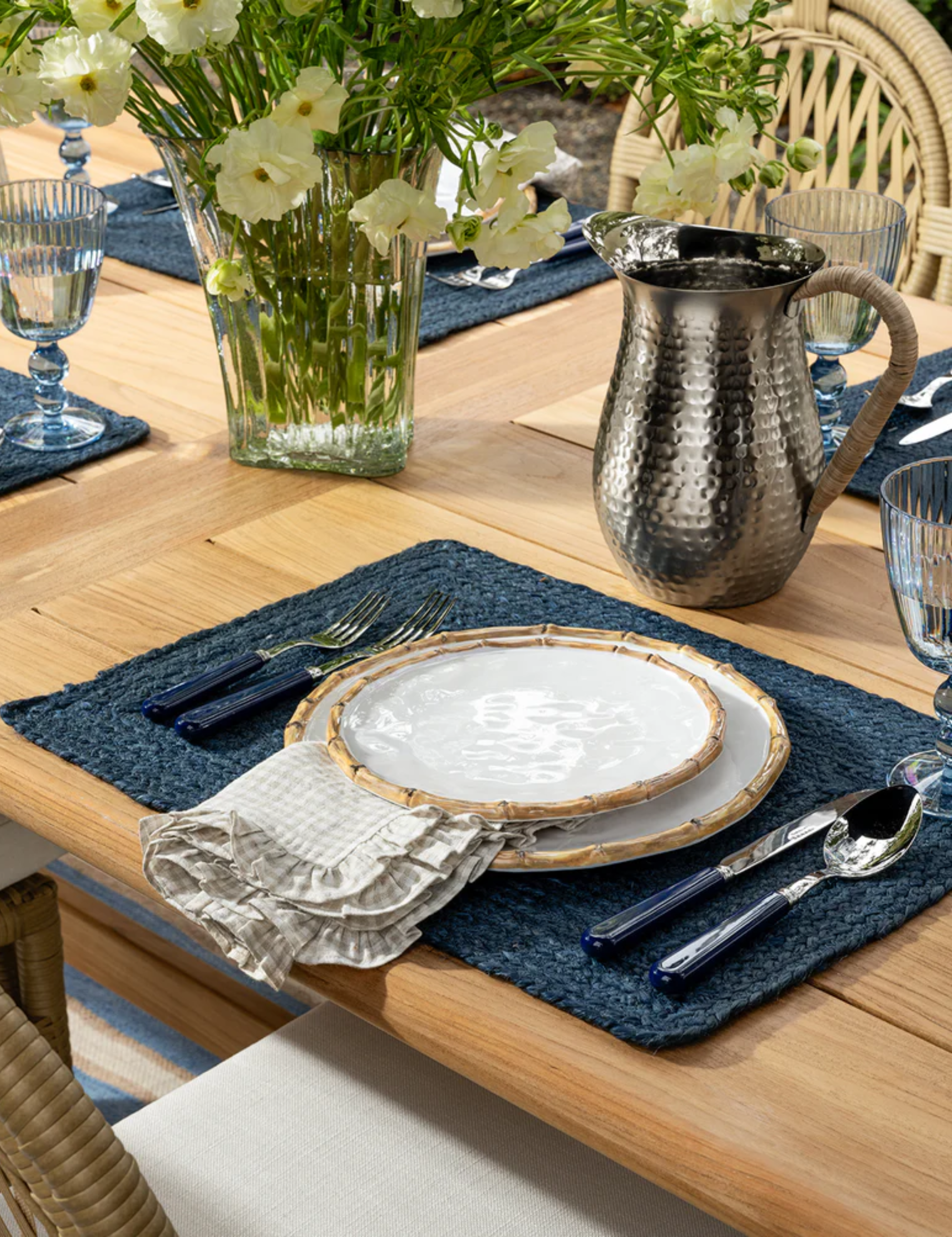 Bamboo plates styled alongside gingham napkin linen, navy placemat, and coordinating navy flatware atop of a wooden dining table