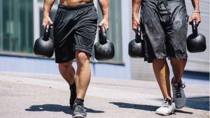 Two men doing a farmer&#039;s carry holding two kettlebells