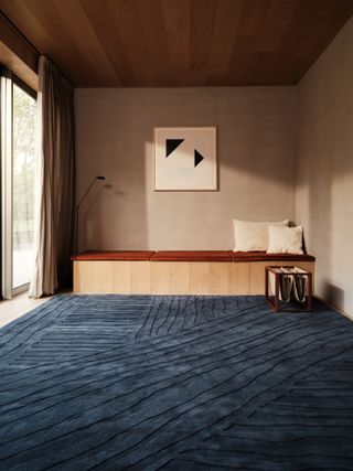 Room with beige walls, built-in wooden bench and inky blue rug carpet