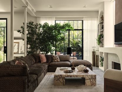 A living room with a brown sofa, a marble coffee table, and a large tree 